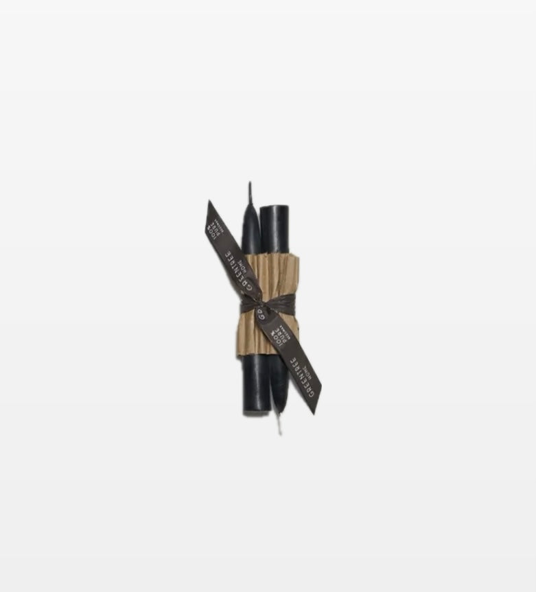 A pair of black candle tapers tied together with a black ribbon, against a white background.