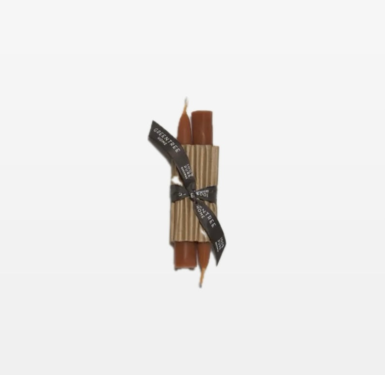A pair of amber candle tapers tied together with a black ribbon, against a white background.