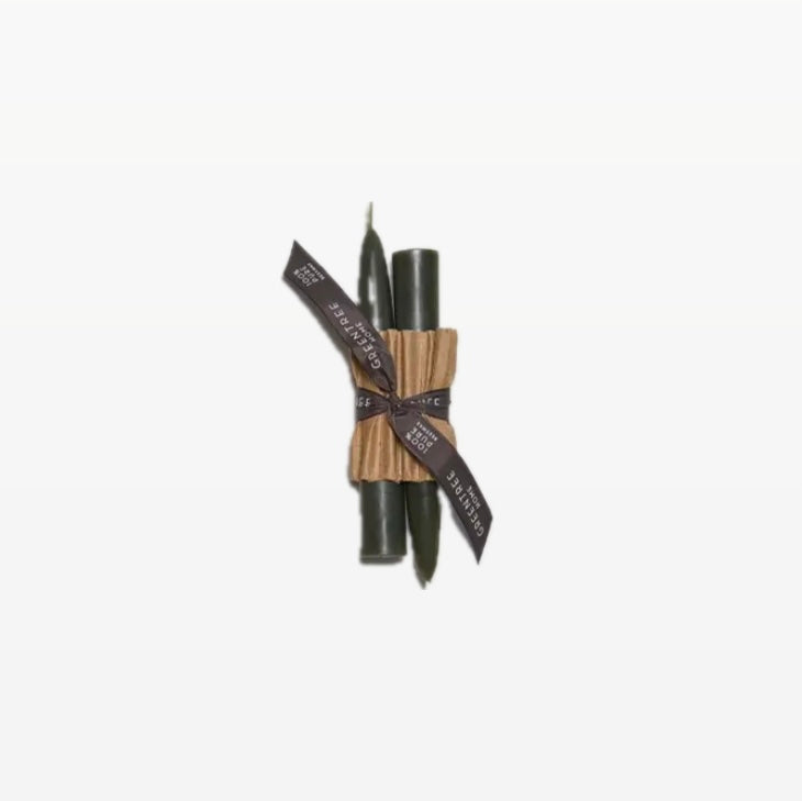 A pair of forest candle tapers tied together with a black ribbon, against a white background.