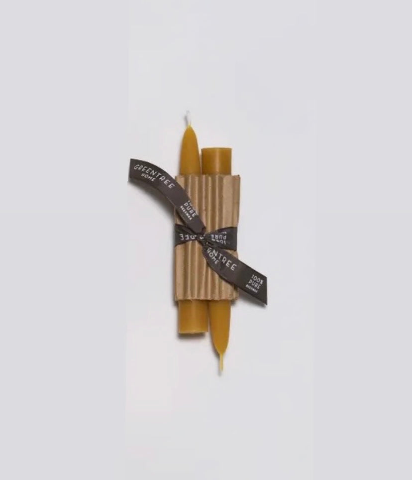 A pair of beige candle tapers tied together with a black ribbon, against a white background.