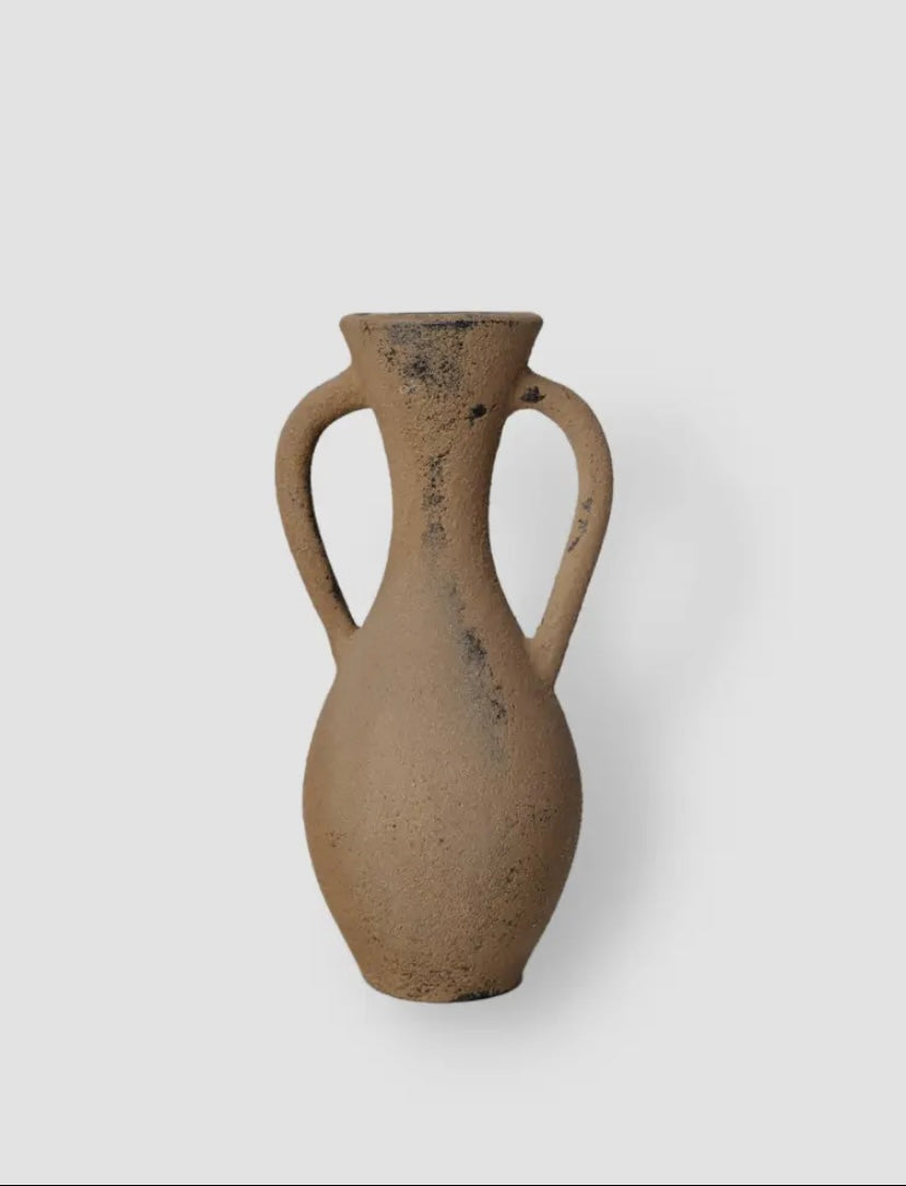 The handmade Amil ceramic vase features a rustic umber tone and textured design, with two handles and a narrow neck.