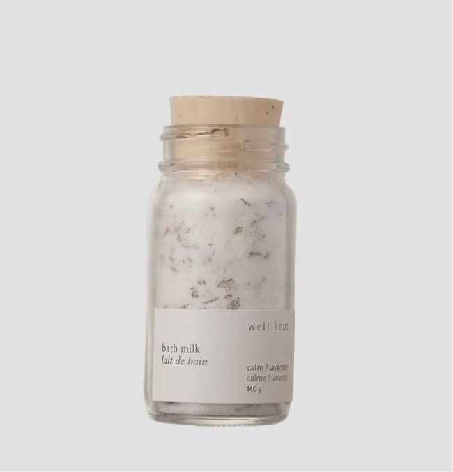 A glass jar containing bath milk with a label that reads 'BATH MILK calm/lavender'. The jar has a wooden lid and is placed against a white background.