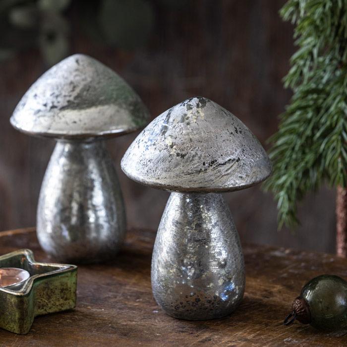 Two metallic mushroom decorations on a wooden surface with an evergreen background