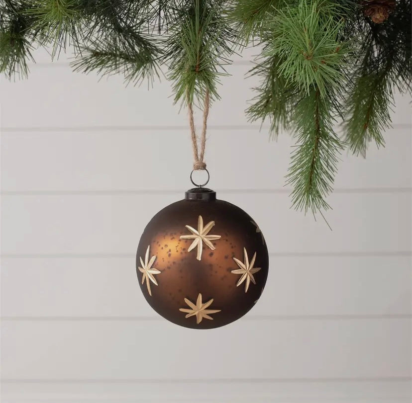 Decorative Christmas ornament with star patterns hanging from a tree branch.
