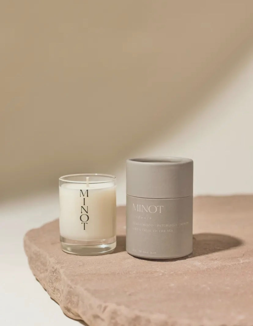 White Cliffwalk candle by MINOT with a gray packaging. This candle features sandlewood and patchouli.