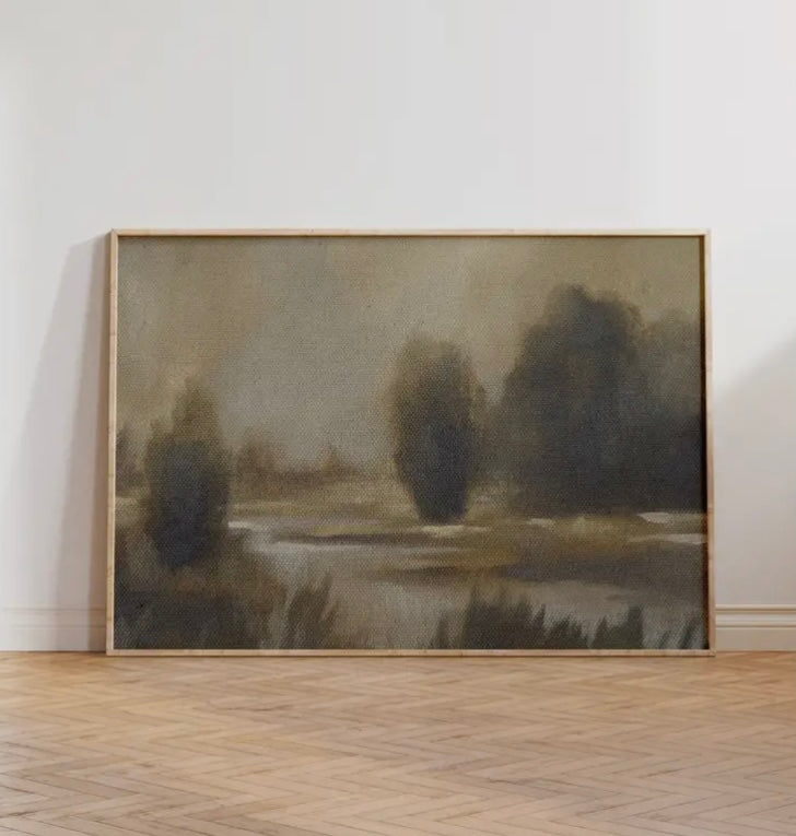 Framed landscape painting of a lake with trees on a white wall.