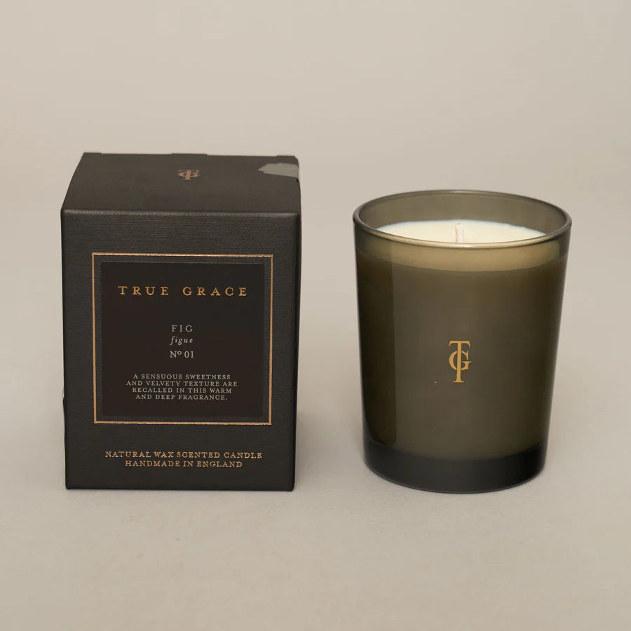 A dark glass candle with 'True Grace' and 'Fig No.01' branding, accompanied by its black packaging box with the product name and description.
