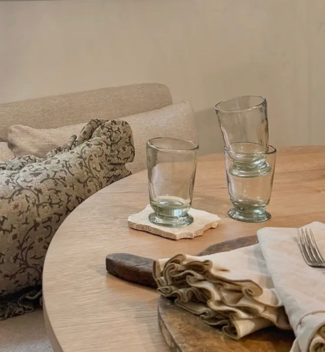 Round wooden table with glasses, napkins, and cutlery in a cozy living room setting.