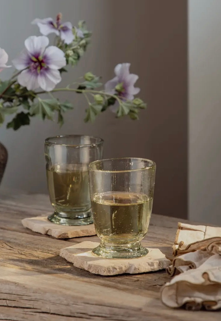 Two glasses of tea on a wooden table with flowers in the background