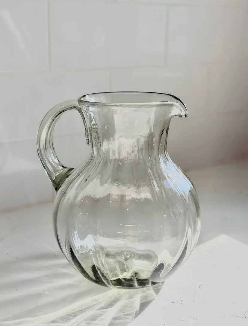 Clear glass pitcher on a white surface with a white tiled wall background