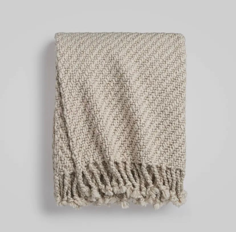 Textured beige throw blanket with fringes on a light gray background