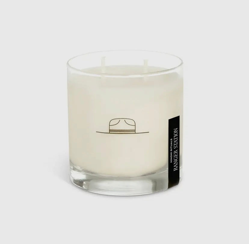 Candle in a glass container with a label featuring a hat design on a white background