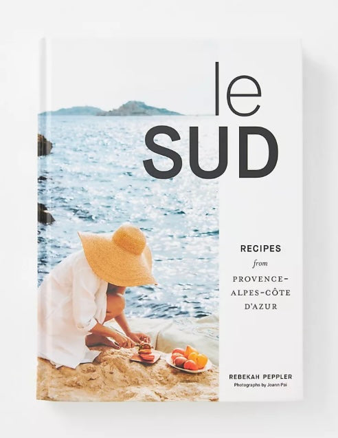 Cookbook cover for 'Le Sud' featuring a photograph of a woman relaxing by the sea with a book in her hand, titled 'Recipes from Provence-Alpes-Cote d'Azur'.