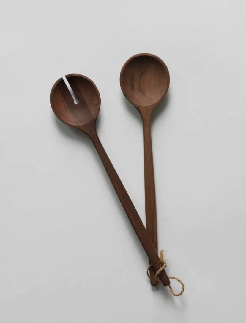 A pair of walnut wooden salad servers hanging on a wall, with one server slightly in front of the other.