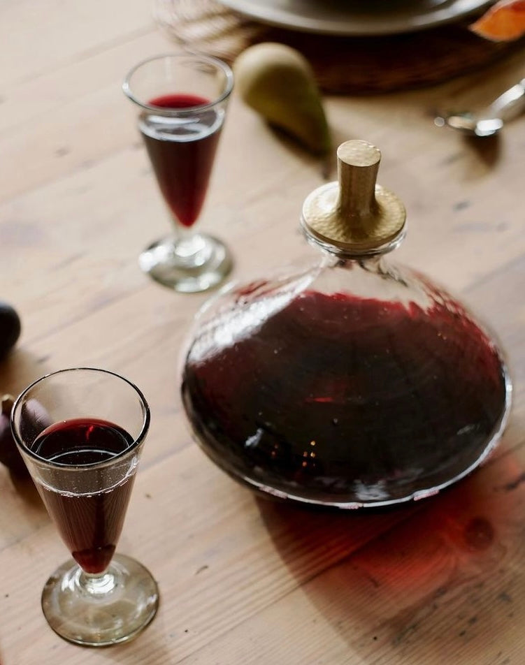 Wide hammered glass decanter filled with red wine on a table with two filled port glasses.