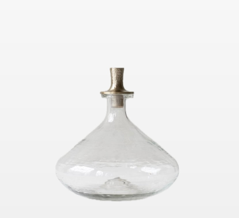 A clear glass decanter with a hand-blown pebbled texture and a metallic stopper with an antiqued brass finish.