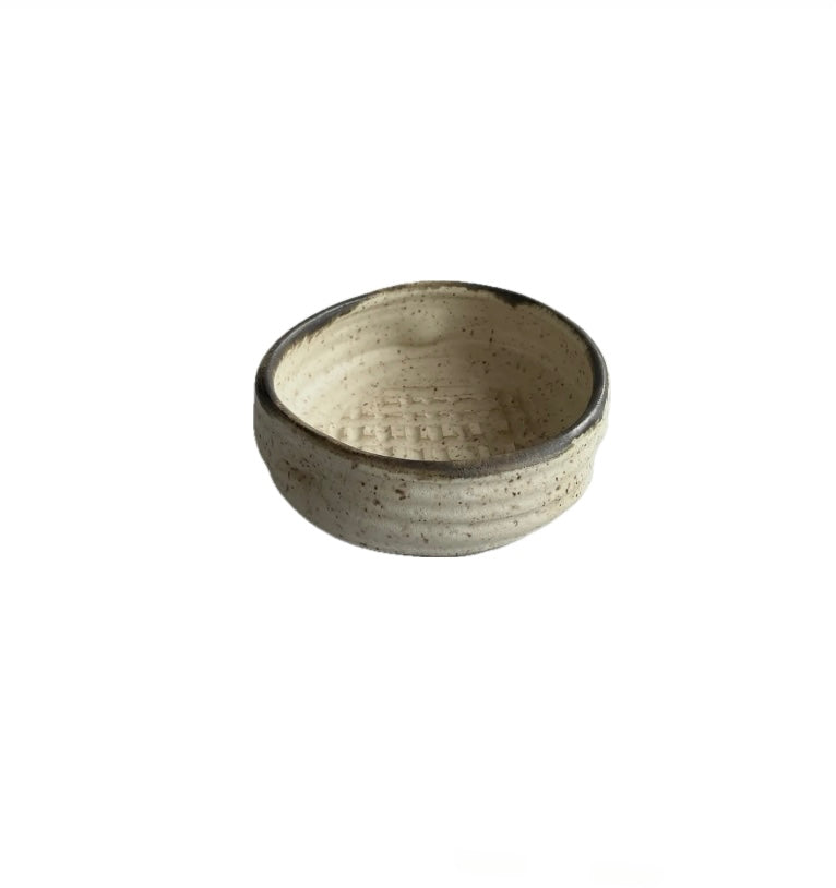 A beige ceramic garlic grater bowl with brown accents at the lip, on a white background.