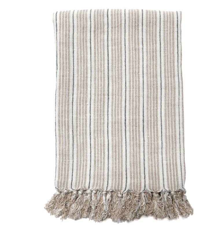 A striped linen throw with tassels on the edge, featuring natural and midnight stripes, displayed on a white background.