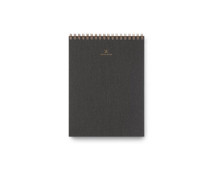 A charcoal, top-bound notepad with a waterproof cotton bookcloth cover and brass wire-o binding.
