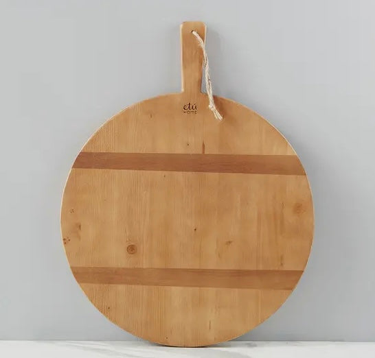 A round pine charcuterie board from Etu Home with two strips of contrasting timber on one side, hanging on a wall hook.