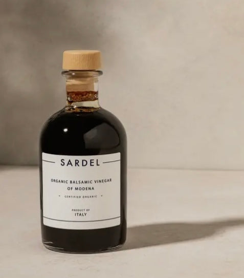 A bottle of Sardel Organic Balsamic Vinegar with a white label and wooden cap, on a neutral background.