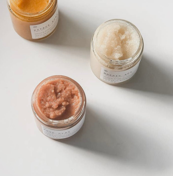 Four jars of ORGANIC SUGAR SCRUB, two with a rose clay texture and two with a nordic spa texture, on a light background.