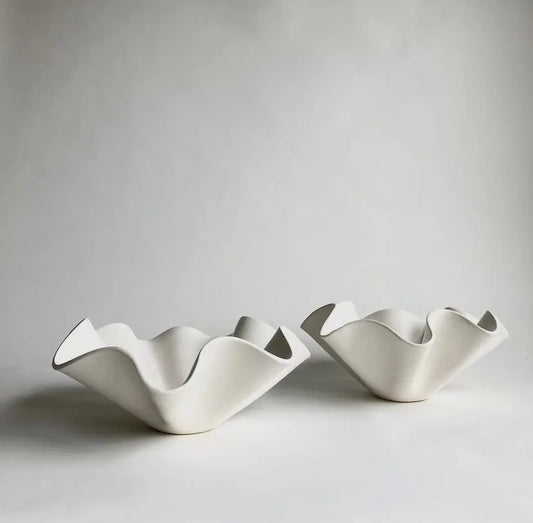 Two white ceramic ruffle bowls of different sizes placed on a neutral surface.