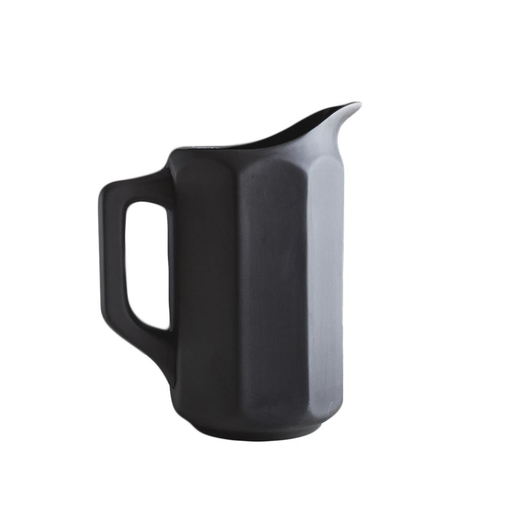 Large black ceramic pitcher on a with octagonal paneled sides.