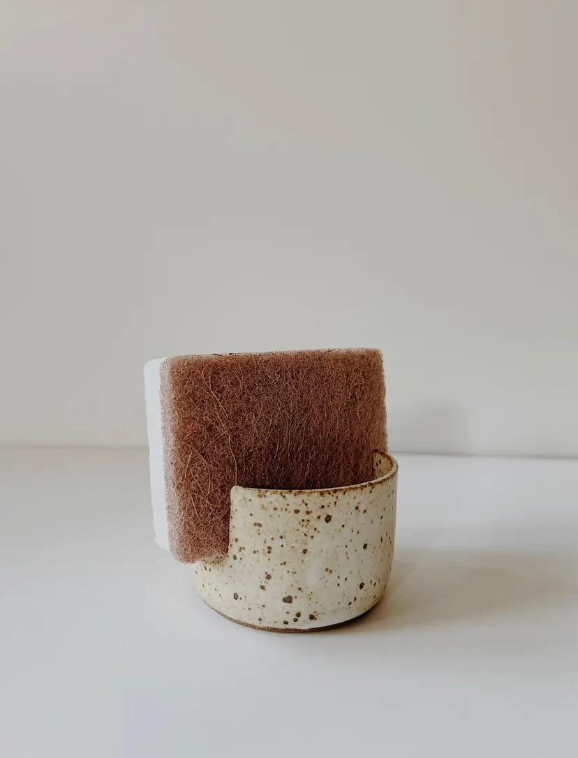 Speckled ceramic sponge holder with a brown sponge.