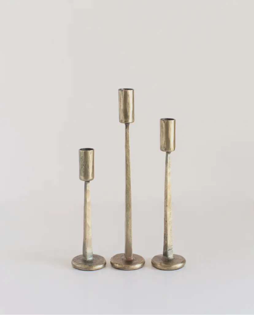 Three heavy brass candle holders of different heights on a light gray background
