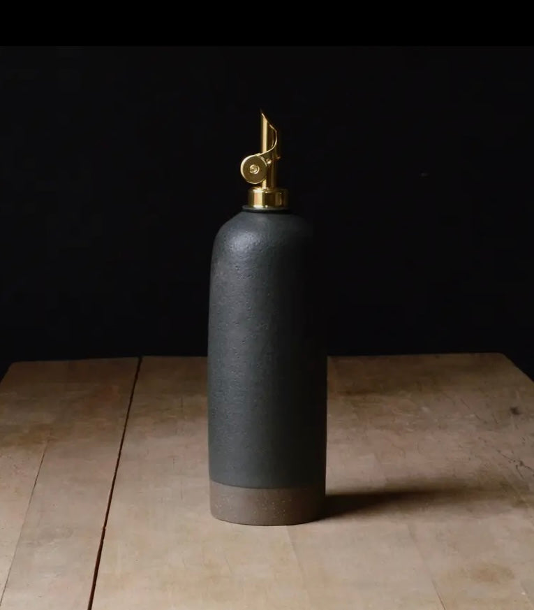 Black ceramic oil bottle with gold spout on a wooden table.