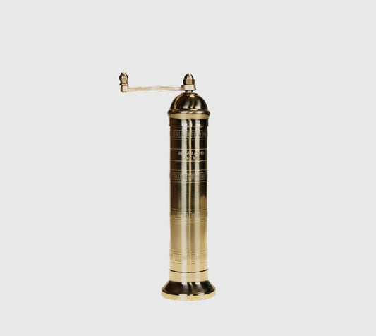 A tall brass salt mill with a crank on top, standing against a white background.