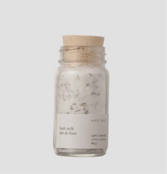 A glass jar containing bath milk with a label that reads 'BATH MILK calm/lavender'. The jar has a wooden lid and is placed against a white background.