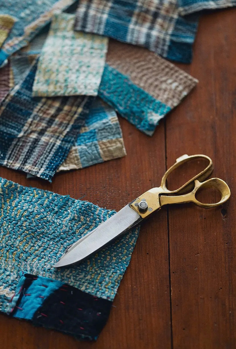 Gold-handled scissors on a wooden surface with fabric pieces