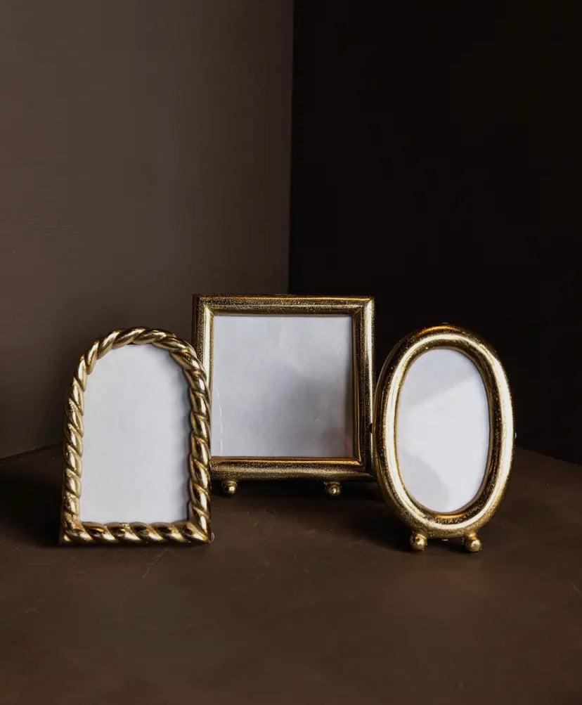 Three gold photo frames of different shapes on a shelf - arch, square, oval.