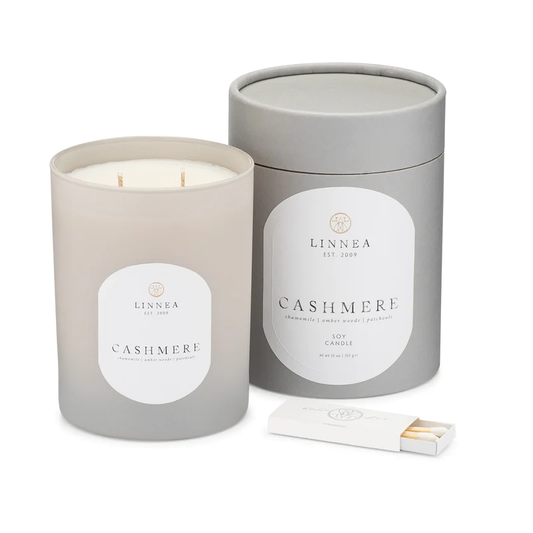 A soy candle from LINNEA, in a grey container with a white label, next to a gray lid and a matchbox.