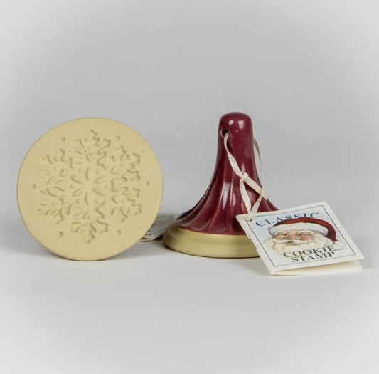Cookie stamp with a round beige stamp and a red handle on a light gray background.