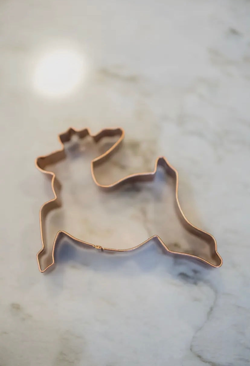 Copper reindeer-shaped cookie cutter on a marble surface