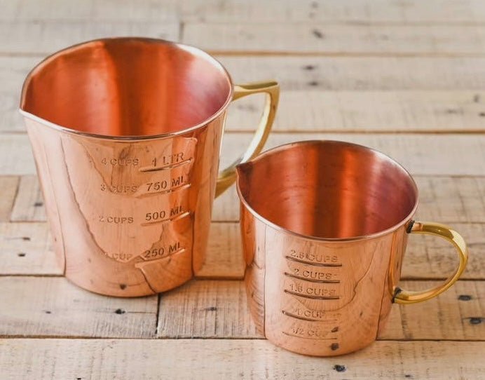 Small and Large coper measuring cups on a wooden table.