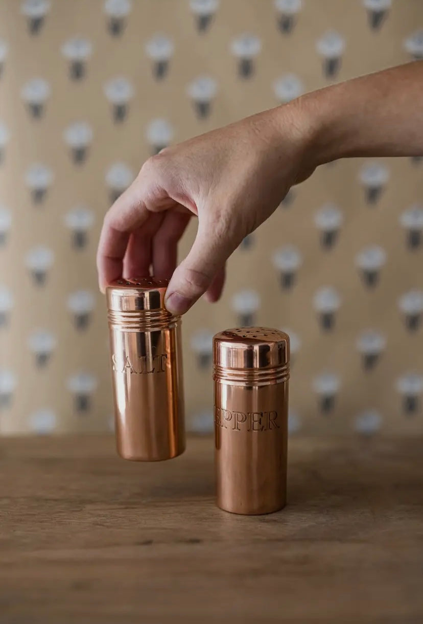 Copper shakers with 'Copper' branding held by a hand against a patterned background