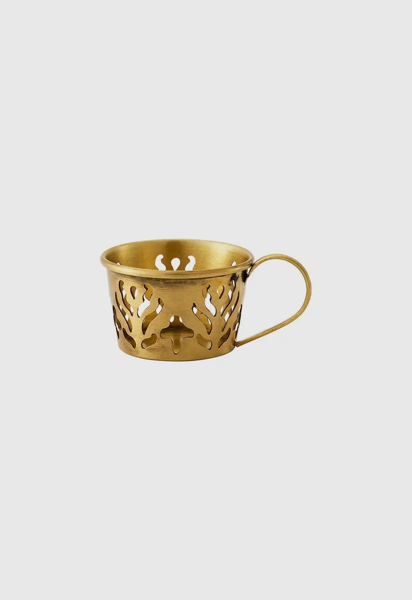 Gold decorative cup that serves as a candle holder with intricate cut-out design on a light gray background