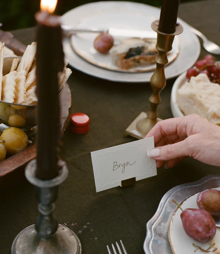 Hand placing a name card on a table setting with candles and food.