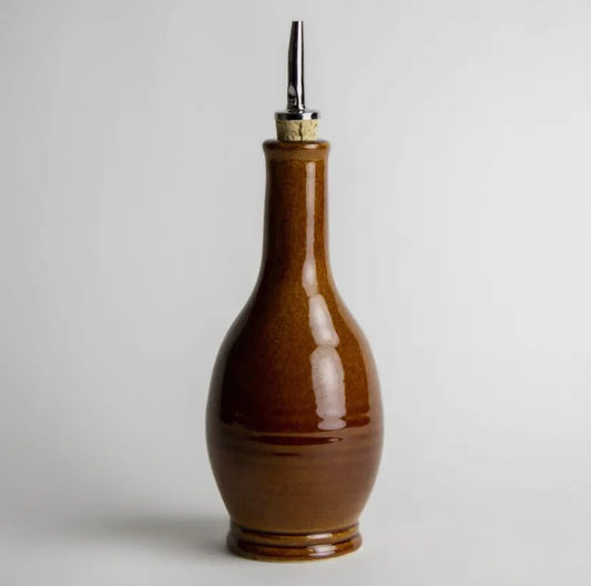 Brown ceramic oil bottle with a metallic nozzle on a light gray background