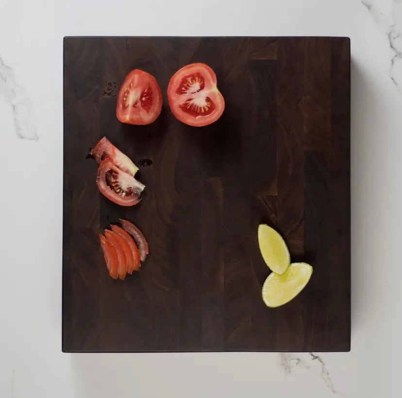 Sliced tomatoes and a yellow fruit on a black walnut butcher block viewed from above.