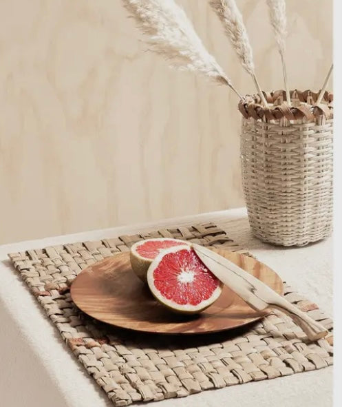 Wooden plate with half a grapefruit and a knife on an ennea woven placemat, with a woven basket in the background.