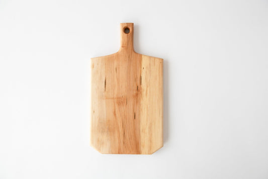 A medium-sized, beige-colored wooden cutting board with a handle, displayed on a white background.