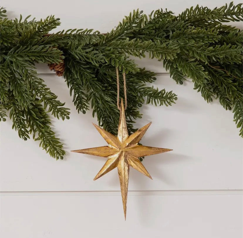 Gold star mango wood ornament hanging from greenery on a white wooden surface