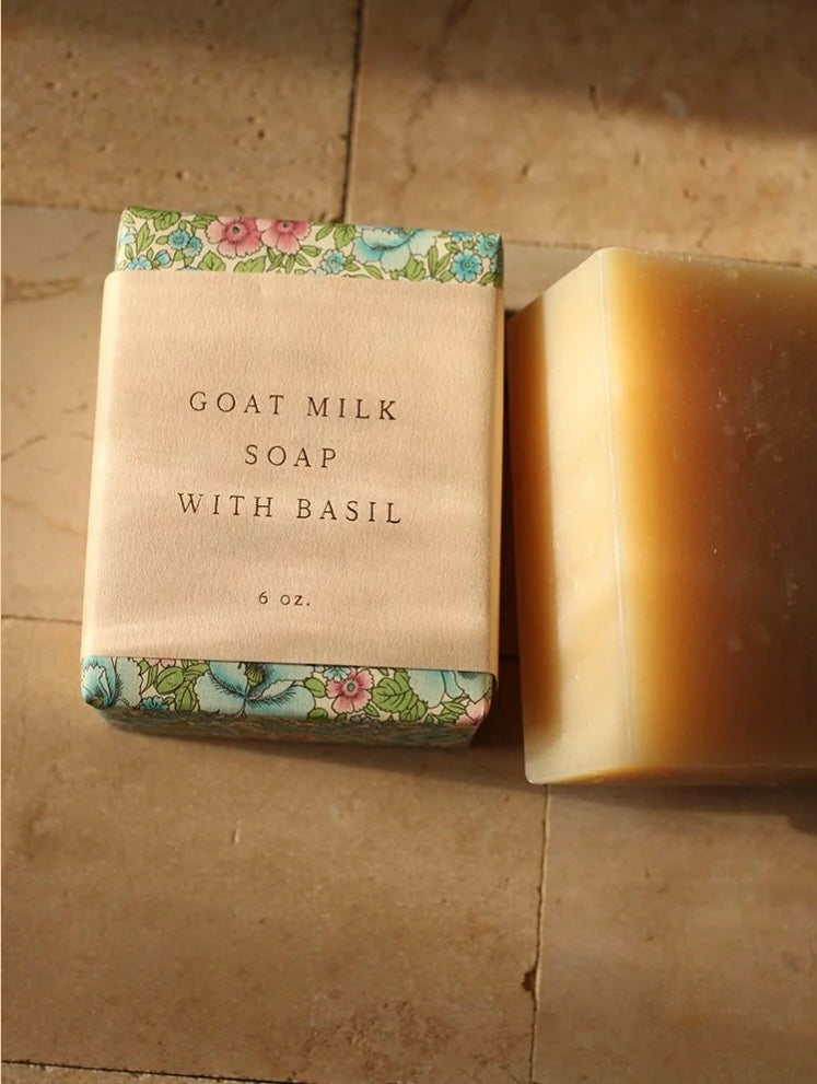 Bar of goat milk soap with basil next to its packaging on a tiled surface