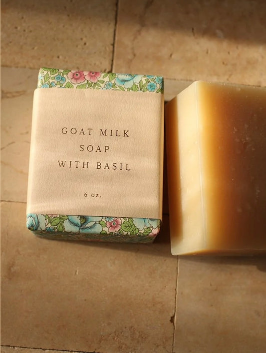 Bar of goat milk soap with basil next to its packaging on a tiled surface