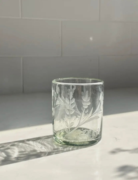 Clear glass tumbler with floral etching on a light surface with a tiled wall background